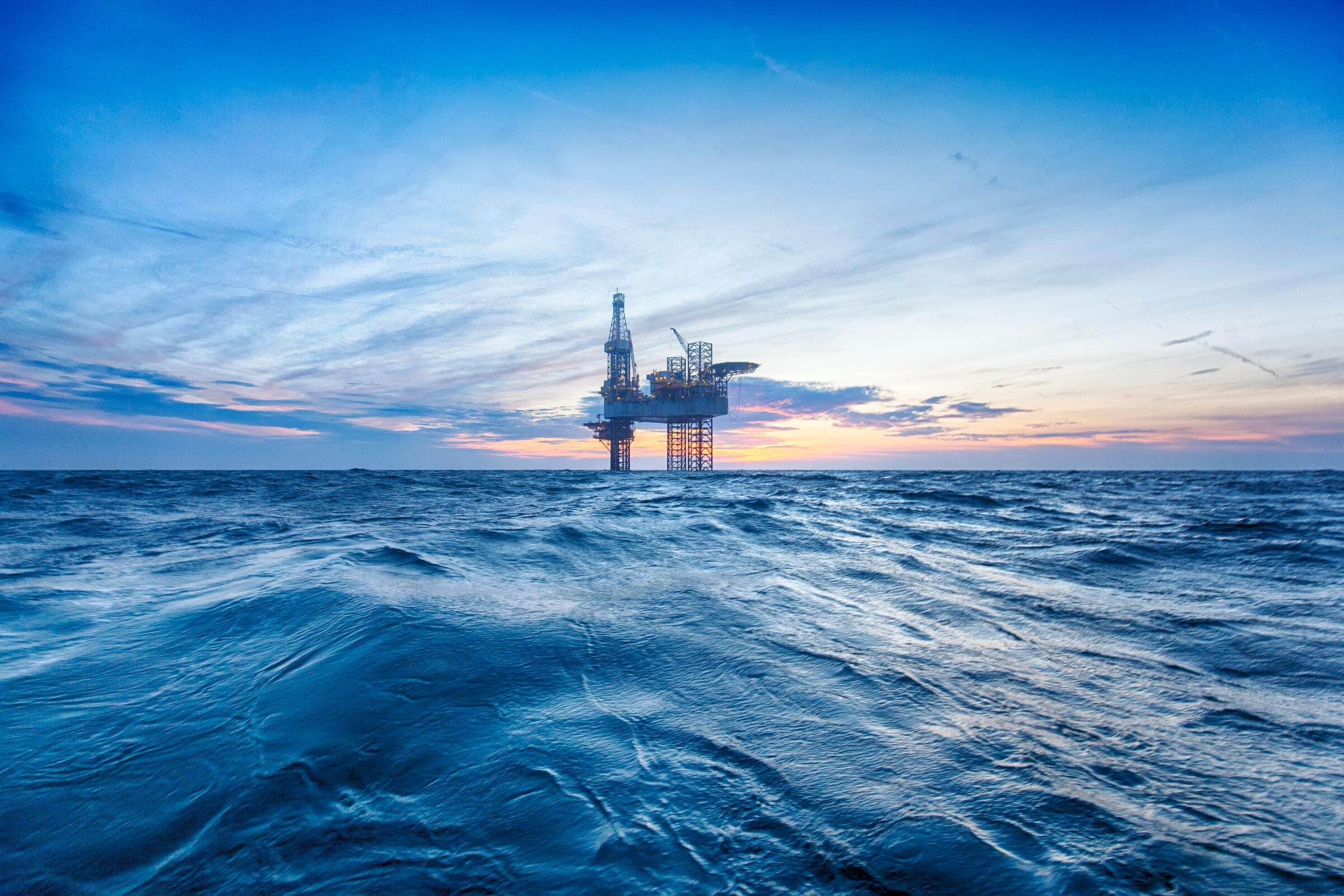 An offshore rig at dusk over a blue sea