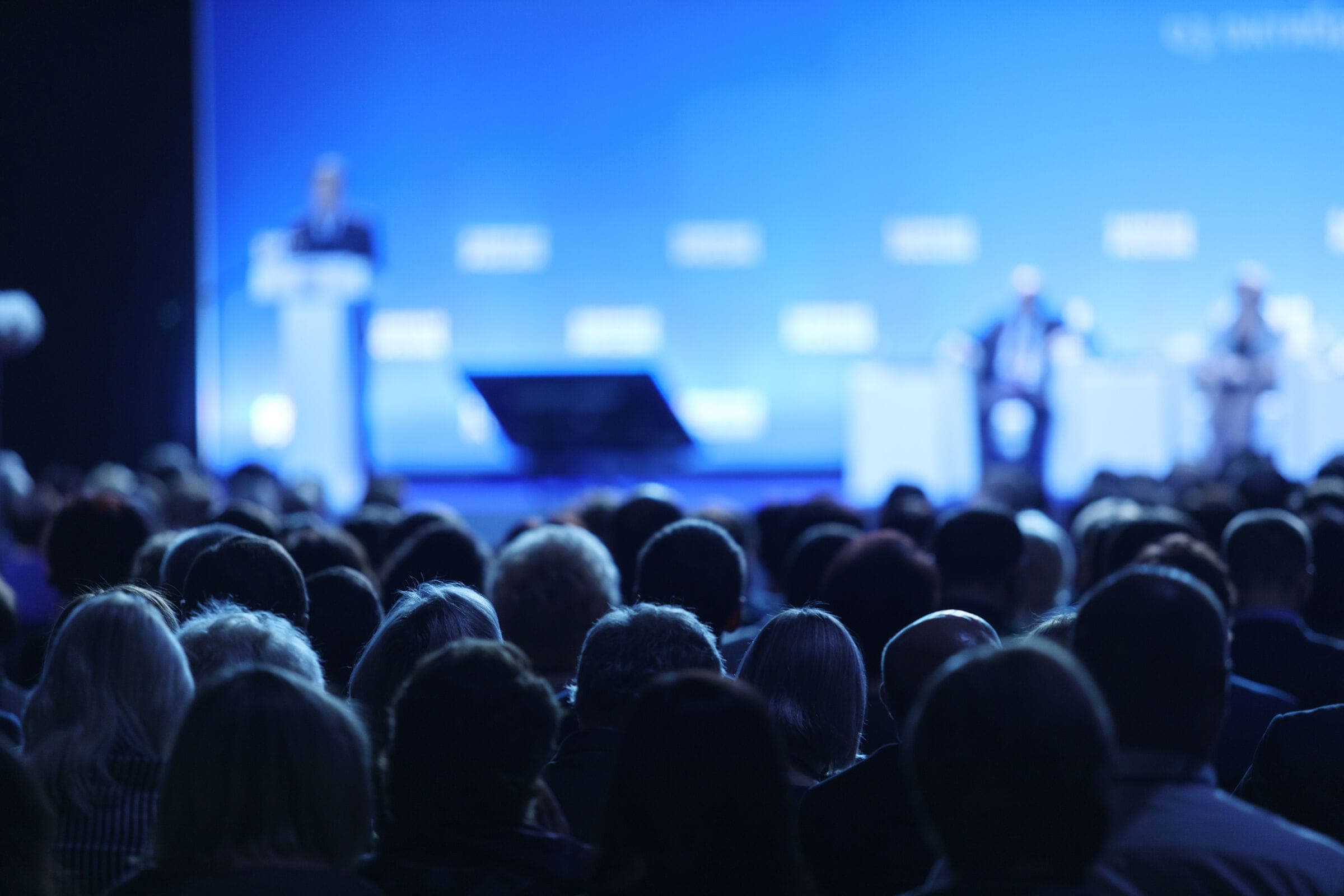 A conference audience facing a blue-lit stage